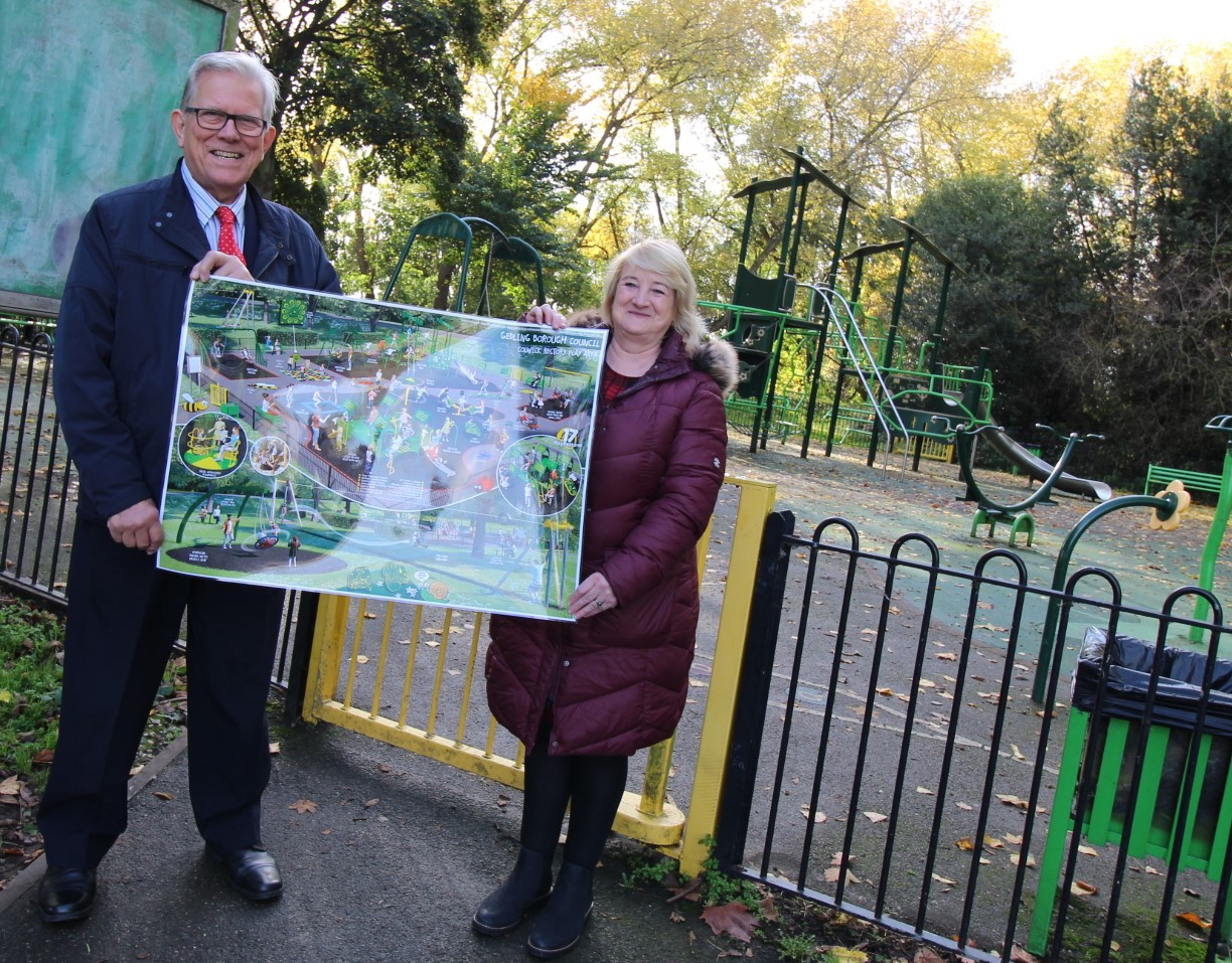 Leadrer of Gedling Borough Council, Cllr John Clarke MBE, with Alison Nunn Chair of Colwick Parish Council, stood outside Colwick Rectory Play Area holding a large laminate of plans for refurbishment works
